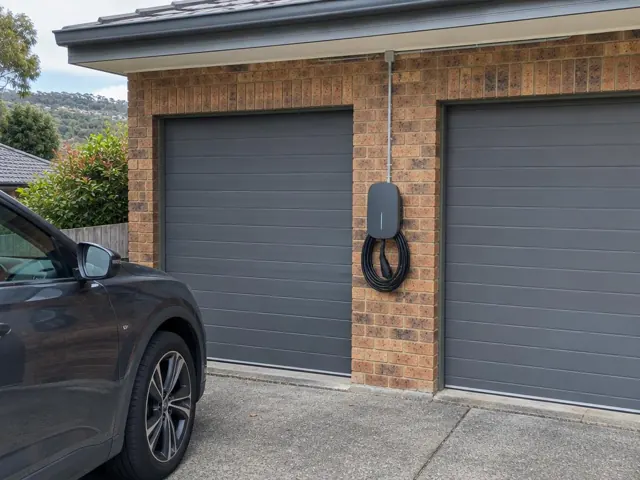 EV charger mounted on a brick wall beside double garage doors and a parked car in Berowra